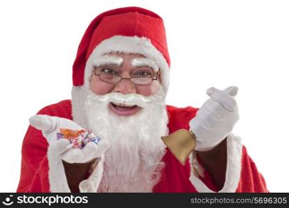 Close-up of happy Santa giving chocolates with bell in hand over white background