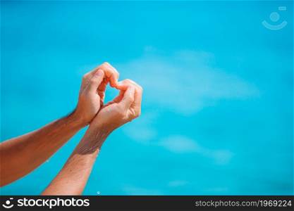 Close up of heart made by female hands background the turquoise ocean. Female hands in the form of heart against the turquoise sea
