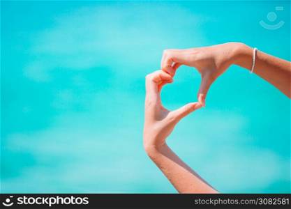 Close up of heart made by female hands background the turquoise ocean. Female hands in the form of heart against the turquoise sea