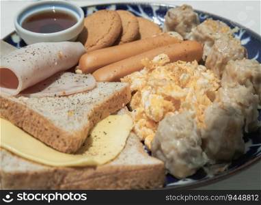 Close-up of Homemade breakfast is including Breads, Fried sausages, Ham, Pork shumais, Scrambled eggs, Cheese, Crispy ginger cookies and Honey on Ceramic plate. Healthy food concept, Selective Focus.