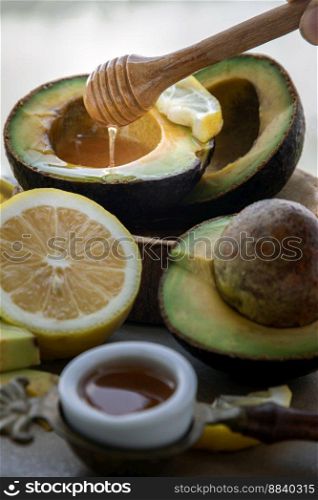 Close-up of Honey dripping from wooden stick dripper into on Fresh organic avocado sliced in half and lemon sliced with honey on Ceramic tray. Healthy food concept, Selective Focus.