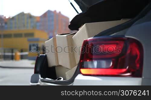 Close up of human hands unloading cardboard boxes from car trunk. Cute young couple unloading their stuff from car trunk while moving to their new apartment.