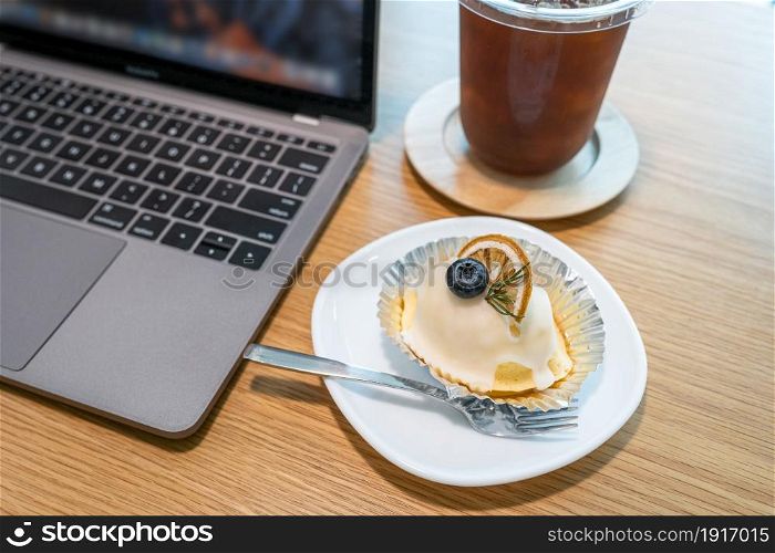 Close-up of ice coffee in cup mug and Homemade white orange cake ?with keyboard laptop computer on wood desk office desk in coffee shop at the cafe,during business work concep