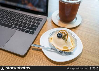 Close-up of ice coffee in cup mug and Homemade white orange cake ?with keyboard laptop computer on wood desk office desk in coffee shop at the cafe,during business work concep
