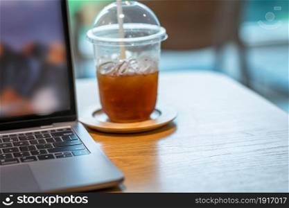 Close-up of ice coffee in cup mug with keyboard laptop computer on wood desk office desk in coffee shop at the cafe,during business work concept