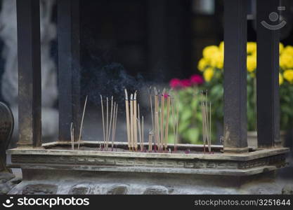 Close-up of incense sticks burning in a decorative urn in a temple