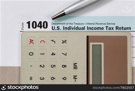 Close up of income tax form, silver pen and calculator with gray folder underneath. Business financial concept.