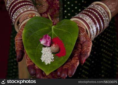 Close-up of Indian bride&rsquo;s hand holding areca nut , flower petal and rice on leaf