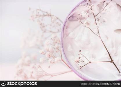 Close up of Jar with cosmetic cream and flowers , natural cosmetic product or beauty concept on pastel background, front view