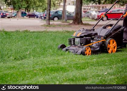 Close-Up Of Lawn Mower On Field. The worker mows the grass on the site, cares for the garden, uses a gasoline lawn mower.. The worker mows the grass on the site, cares for the garden, uses a gasoline lawn mower.
