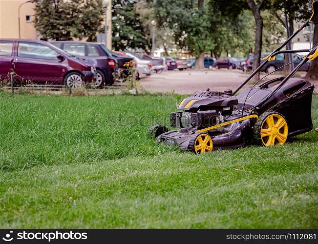 Close-Up Of Lawn Mower On Field. The worker mows the grass on the site, cares for the garden, uses a gasoline lawn mower.. The worker mows the grass on the site, cares for the garden, uses a gasoline lawn mower.