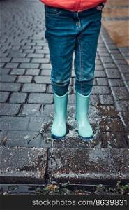 Close up of legs of little girl jumping in puddle wearing rubber boots walking in on rainy gloomy autumn day. Child jumping in puddle wearing rubber boots walking in on rainy gloomy autumn day