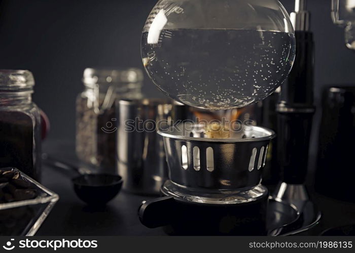 close up of lighter heating vacuum coffee maker also known as vac pot, siphon or syphon coffee maker on rustic black stone table.