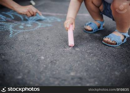 Close up of little girl drawing with chalks on the sidewalk. Kids drawing with chalk. Close up of little girl drawing with chalks on the sidewalk