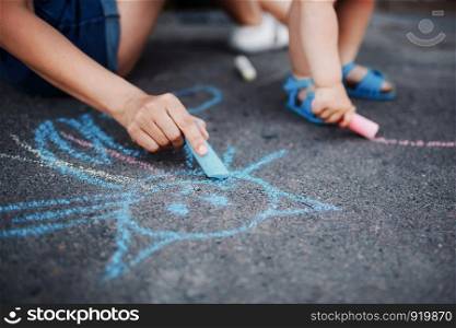 Close up of little girl drawing with chalks on the sidewalk. Kids drawing with chalk. Close up of little girl drawing with chalks on the sidewalk