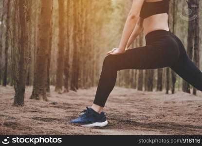 Close up of lower body of woman doing yoga and stretching legs before running in forest at outdoors. Sports and Nature concept. Lifestyle and Activity concept. Pine woods theme.