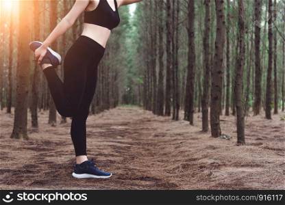 Close up of lower body of woman doing yoga and stretching legs before running in forest at outdoors. Sports and Nature concept. Lifestyle and Activity concept. Pine woods theme.