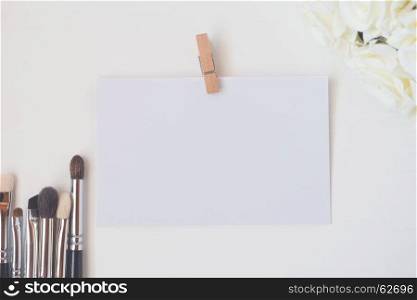 Close-up of makeup brushes with paper card and bucket flowers (color toned image, shallow DOF).