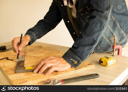 Close-up of male carpenter hands drawing mark on wooden flooring with steel ruler and pencil