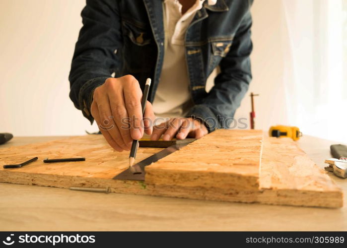 Close-up of male carpenter hands drawing mark on wooden flooring with steel ruler and pencil