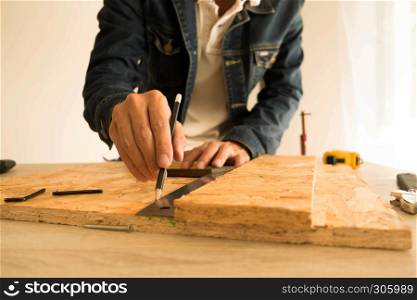 Close-up of male carpenter hands drawing mark on wooden flooring with steel ruler and pencil