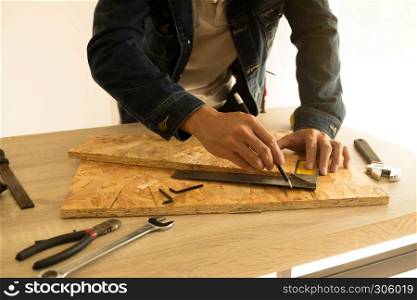 Close-up of male carpenter hands drawing mark on wooden flooring with steel ruler and pencil