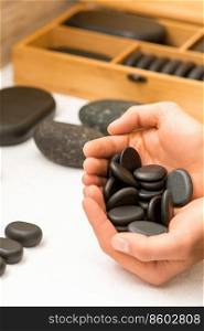 Close up of male hands holding spa black pebbles in her palms over a white table in spa salon. Hands holding spa black pebbles