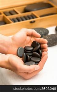 Close up of male hands holding spa black pebbles in her palms over a white table in spa salon. Hands holding spa black pebbles
