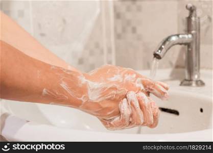 Close-up of male washing hands rubbing with soap over sink in bathroom at home. Hygiene concept