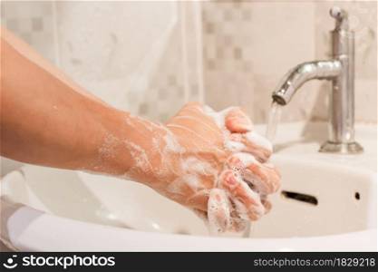 Close-up of male washing hands rubbing with soap over sink in bathroom at home. Hygiene concept