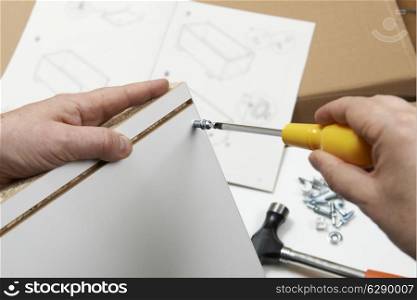 Close Up Of Man Assembling Flat Pack Furniture With Screwdriver