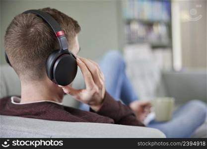 Close Up Of Man At Home Wearing Wireless Headphones Relaxing On Sofa Streaming Music OrListening To Podcast