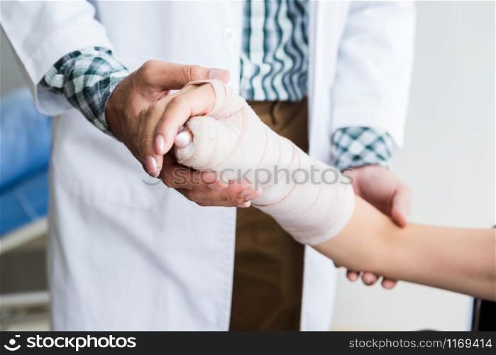 Close-up of man doctor of checking splint the arm of female patient hand due to with her arm broken for better healing with a smile sit in a wheelchair In the room hospital background.