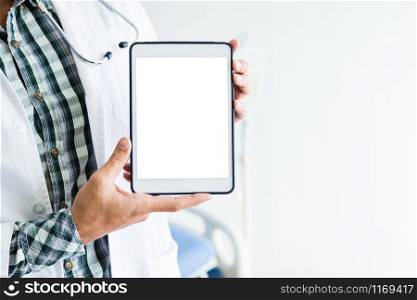 Close-up of man doctor therapeutic advising with positive emotions holding up and showing digital tablet with a blank white screen and bed in hospital background,copy space