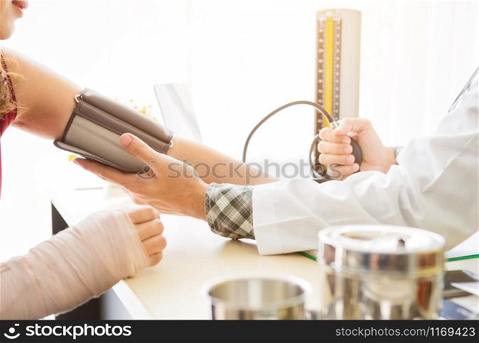 Close-up of man doctor with measuring the pressure to the arm of a female patient wear arm splint with analogue pressure gauge for better healing In the room hospital background.