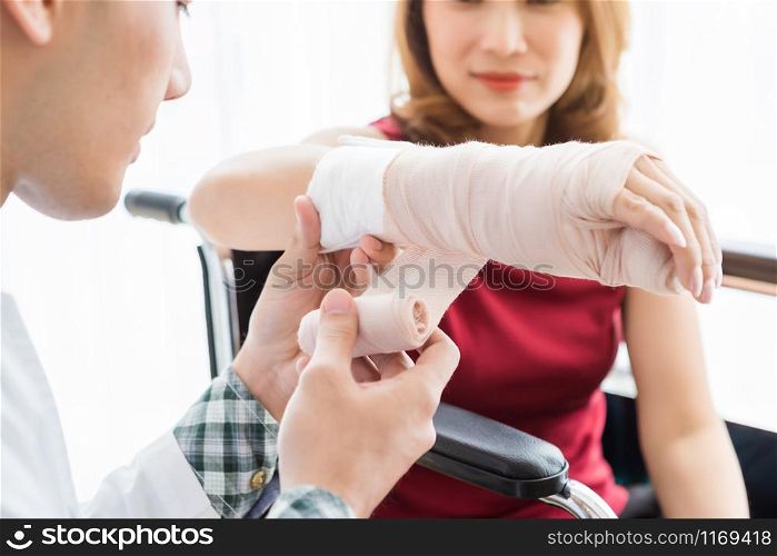 Close-up of man doctor with wrapping nurse bandages splint to the arm of a female patient wear arm splint with analogue pressure gauge for better healing In the room hospital background.