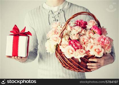 close up of man holding basket full of flowers and gift box.