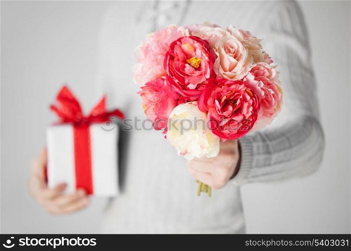 close up of man holding bouquet of flowers and gift box.