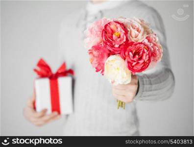 close up of man holding bouquet of flowers and gift box.