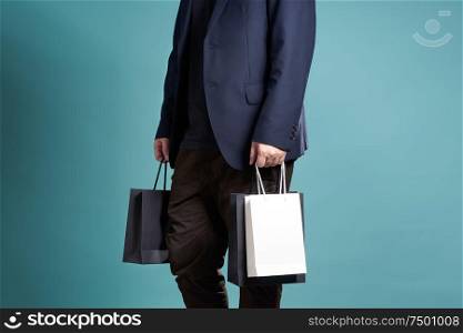 Close up of man in suit with shopping bags , isolated on light blue background .