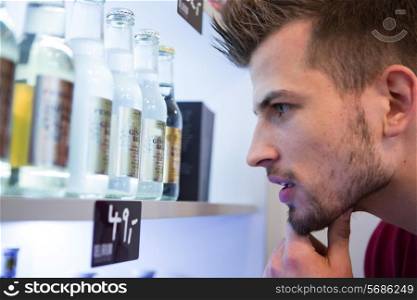 Close-up of man looking at beer bottles displayed on shelf in cafe