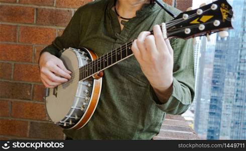 Close Up of Man playing Electric Banjo against Brick Background on Balcony