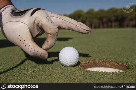 close up of man&rsquo;s hand putting golf ball in hole at course