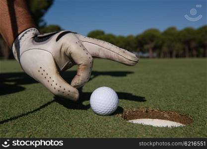 close up of man&rsquo;s hand putting golf ball in hole at course