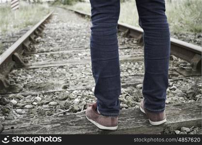 Close-Up Of Man's Feet Standing Between Railway Tracks