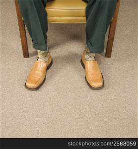 Close up of man sitting in chair wearing retro pants and shoes.
