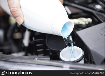 Close-Up Of Man Topping Up Windshield Washer Fluid In Car