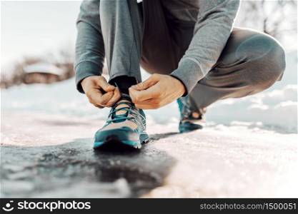 Close up of man tying shoelace while crouching. Winter fitness concept.