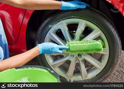 Close Up Of Man Washing Wheels Of Car During Valet Using Bucket And Sponge