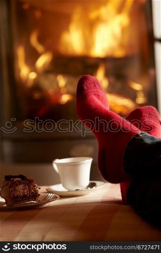 Close Up Of Mans Feet Relaxing By Cosy Log Fire With Tea And Cake